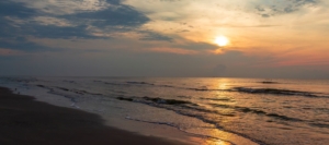 Sunrise over calm ocean waves along a sandy beach with dramatic clouds in the sky