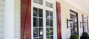 Close-up view of white-framed windows with red shutters and outdoor lanterns on the front porch of a home