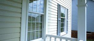 Close-up of a home's beige vinyl siding and double-hung window with blue shutters